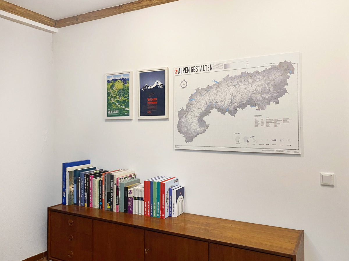 Alpen Gestalten – Wandkarte über einem Sideboard neben zwei gerahmten Bergdrucken